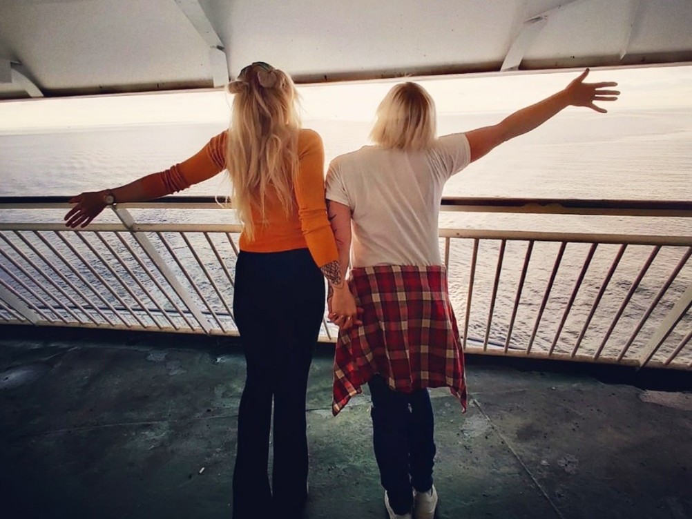 Kaksi nuorta naista selät kohti kameraa, laivan kannella iloisen näköisinä.