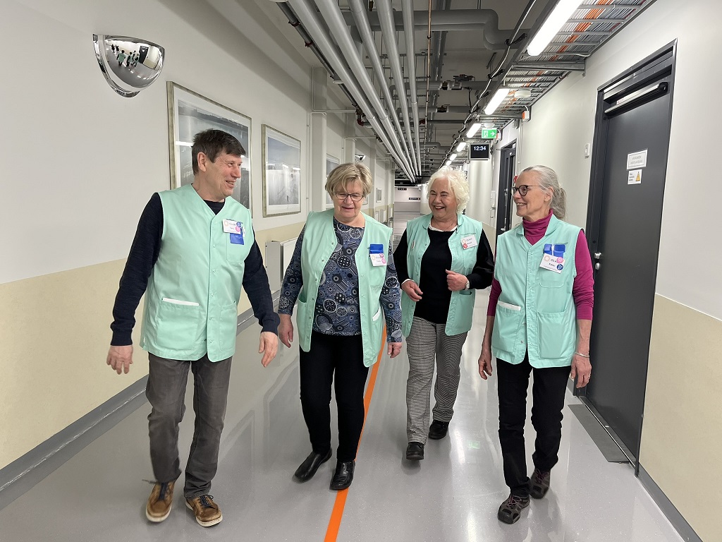 OLKAn vapaaehtoisia sairaalan käytävällä. Vapaaehtoiset kävelevät ja juttelevat hymyillen keskenään.