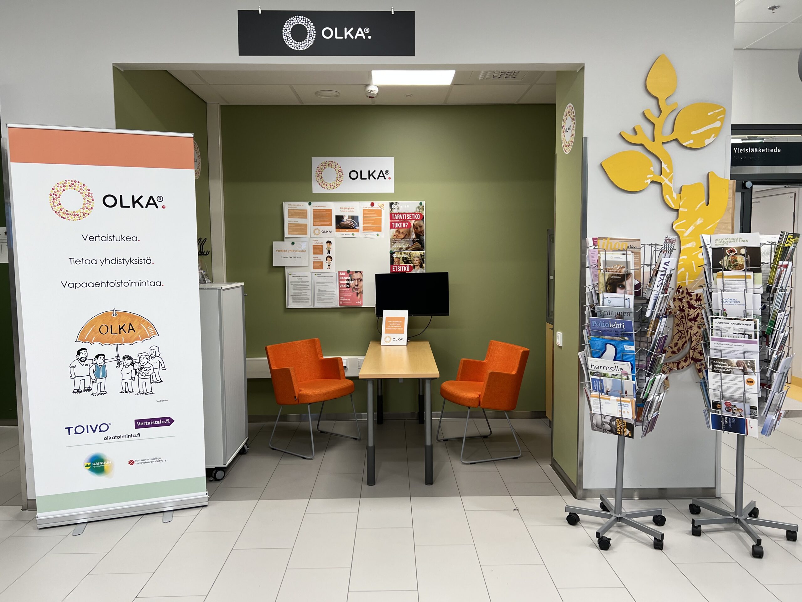 OLKA-piste Kainuun keskussairaalassa. Pisteellä on syvennys, jossa on luku- ja istumatilaa sekä eri järjestöjen esitteitä, lehtiä ja OLKAn roll up.