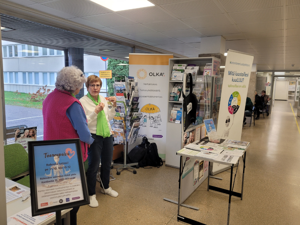 Kuvassa Riihimäen sairaalan OLKA-piste, jolla Kanta-Hämeen luustoyhdistys ry pitää teemapäivää. Kaksi naishenkilöä keskustelee keskenään pisteellä.