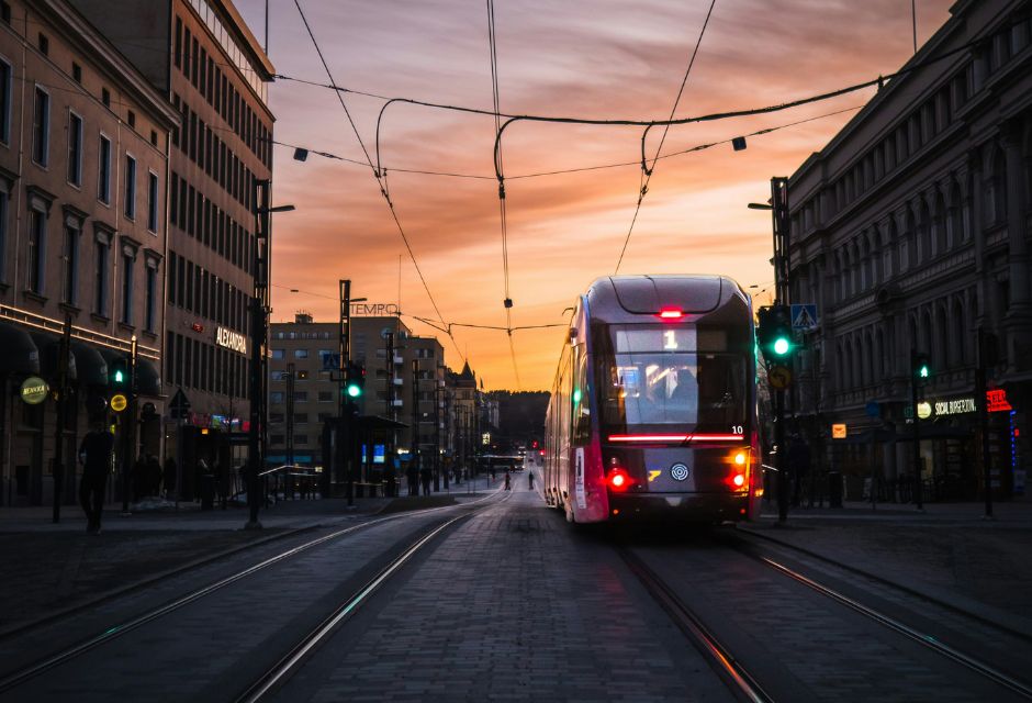 Tampereen keskustanäkymä kesäisessä iltahämärässä, auringonlaskun aikaan. Kadulla kulkee raitiovaunu ja muuta liikennettä.