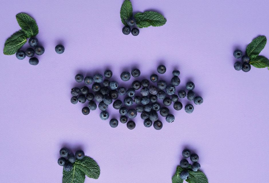 Vaaleanvioletti pohja, jonka päälle on aseteltu mustikoita ja mintunlehtiä pieniin rykelmiin.