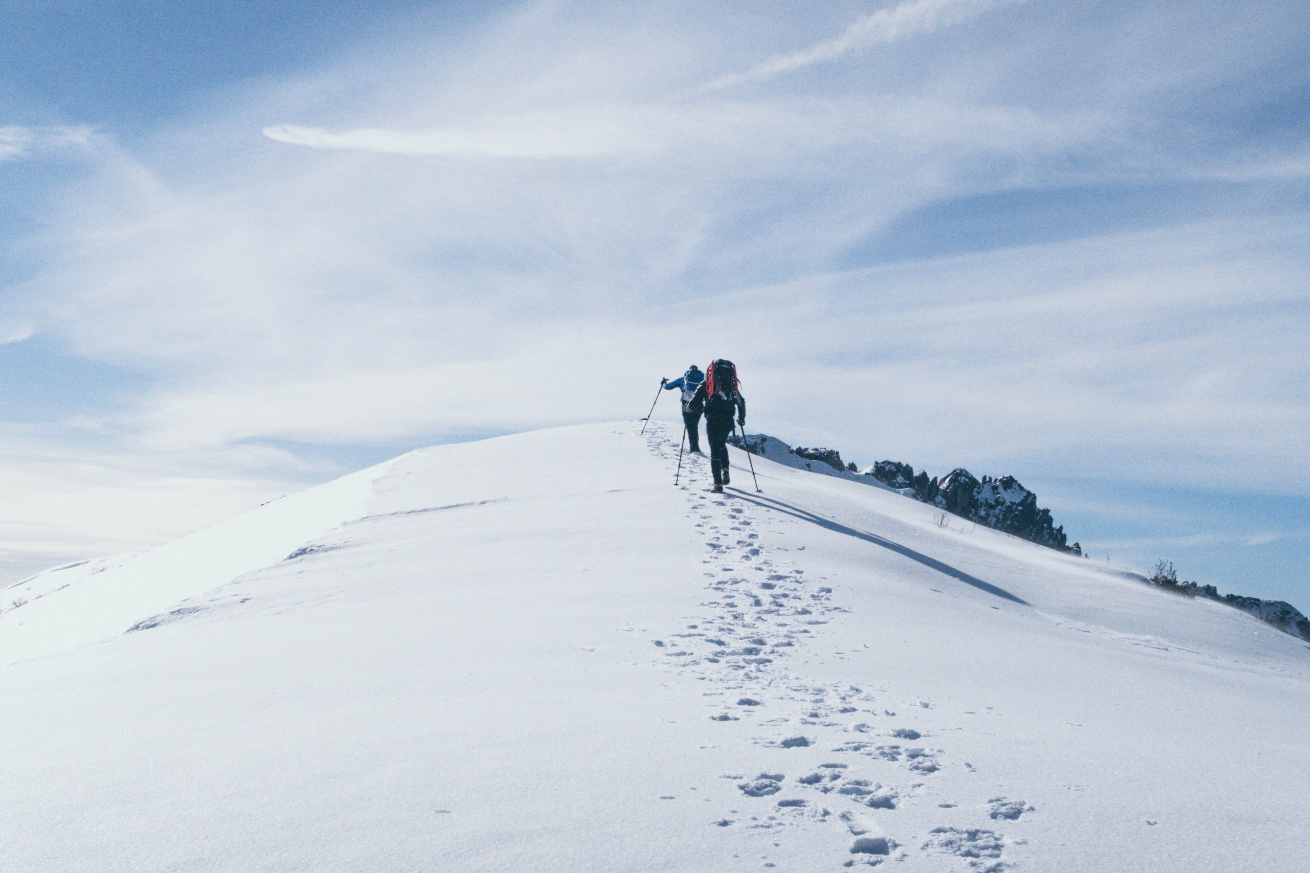 Kaksi ihmistä kipuaa lumisen vuoren huipulle kävellen.
